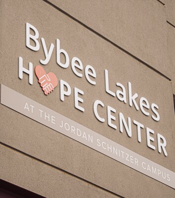 A close-up shot of the sign for "Bybee Lakes Hope Center" with the logo featuring a heart and hands. The text below reads "AT THE JORDAN SCHNITZER CAMPUS."