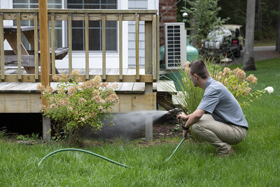 ohDEER technician applying all-natural tick and mosquito control beneath a deck in the backyard of a home.