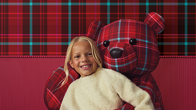 A young girl poses with a festive red-and-blue plaid bear. 